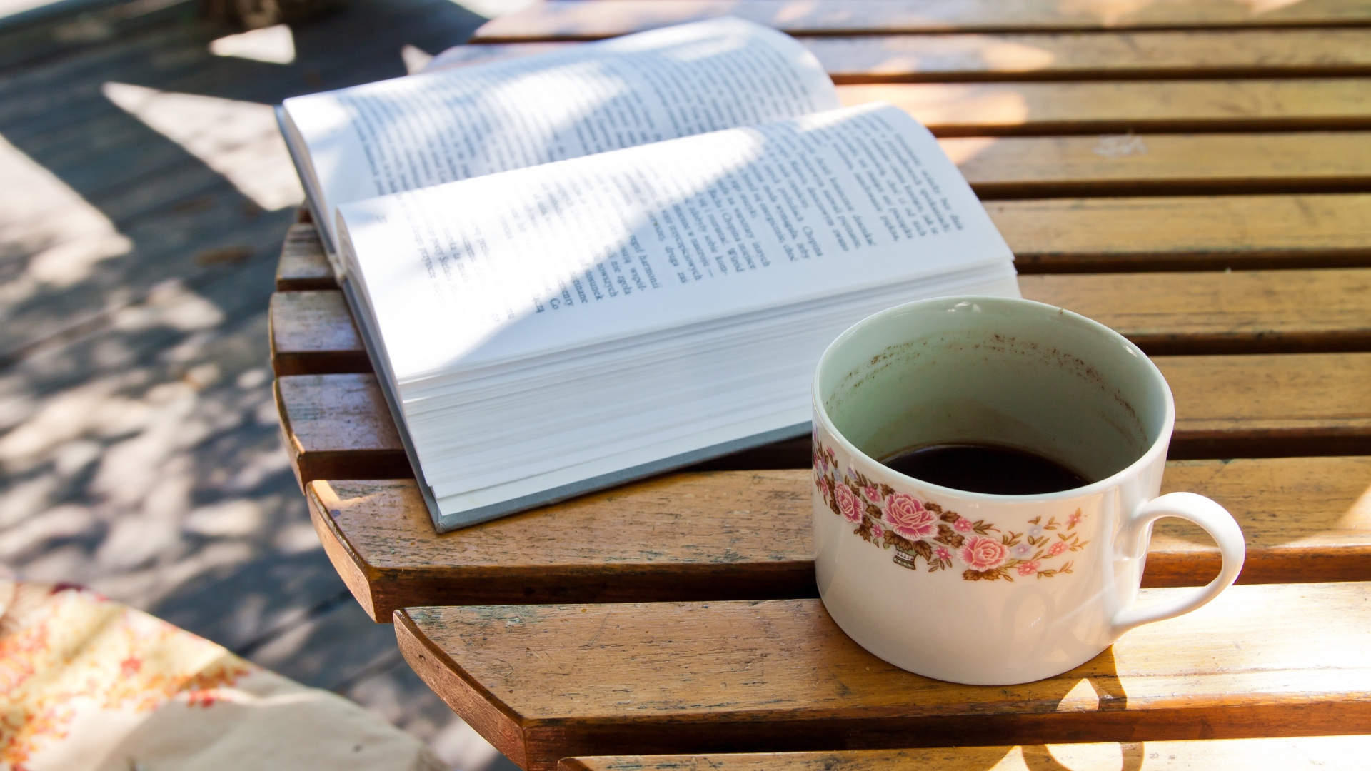 An open book and a cup of coffee on a sunlit café table